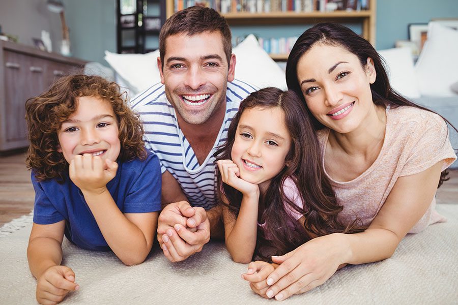 Personal Insurance - Portrait of Smiling Family with Two Kids Laying on the Rug in the Living Room
